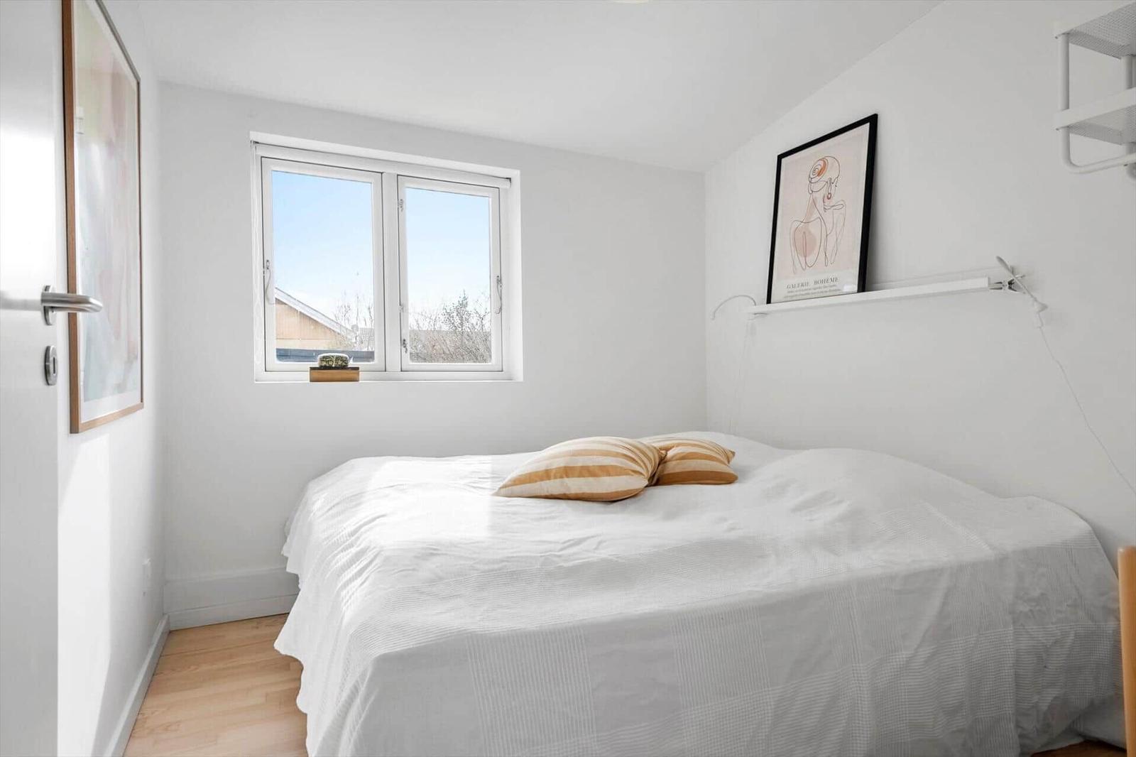 Schlafzimmer mit Bett, Fenster und Wandbildern.