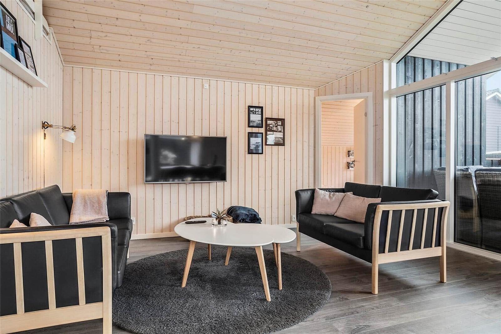 Wohnzimmer mit Holzwänden, zwei schwarzen Sofas und runden Tisch.
