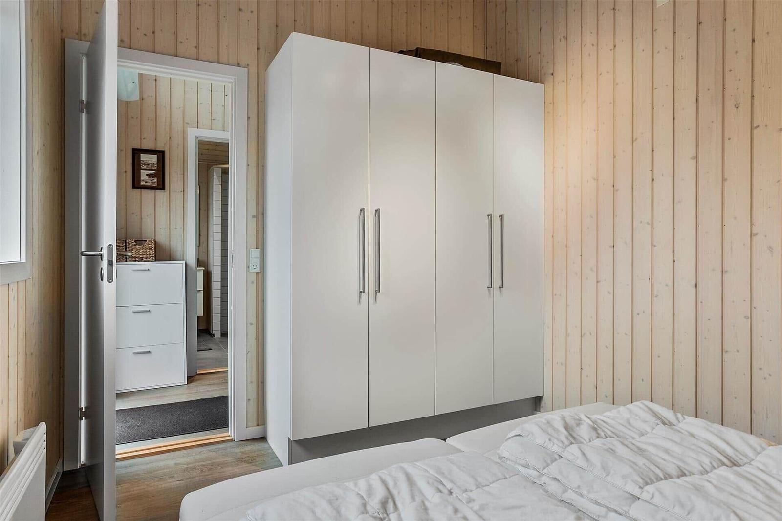 Schlafzimmer mit weißem Schrank und Holzwand. Tür führt in angrenzenden Raum.