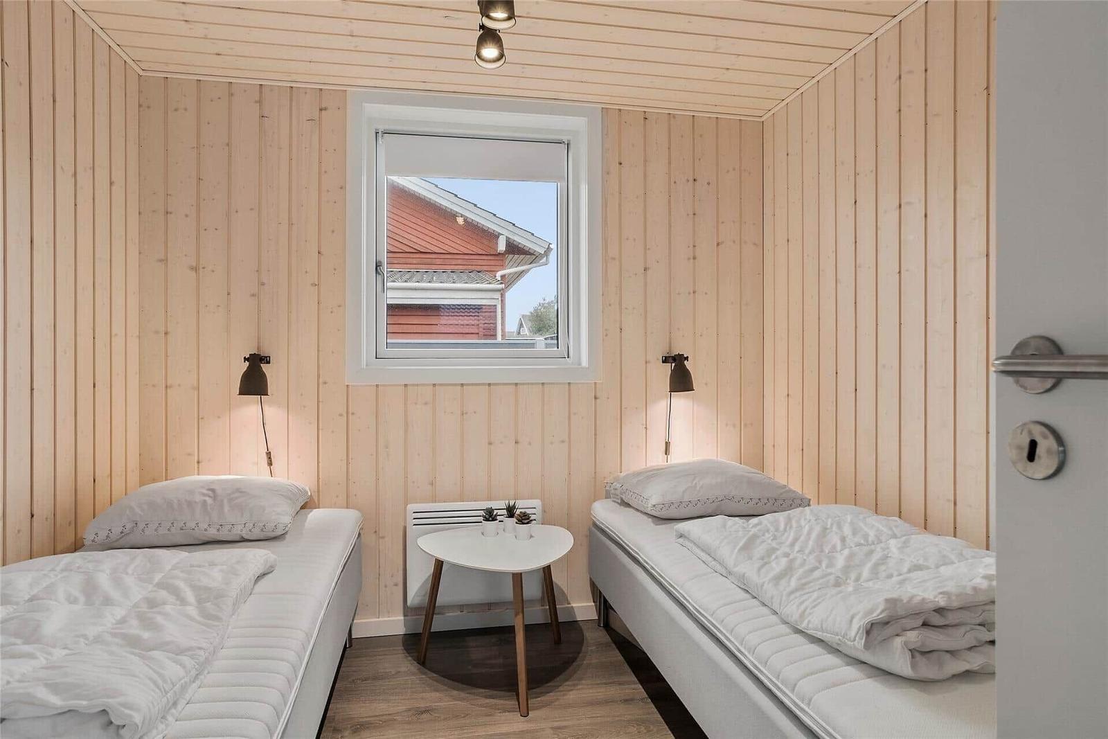 Zwei Betten mit weißen Bettwäschen, Holzwand und Fenster.