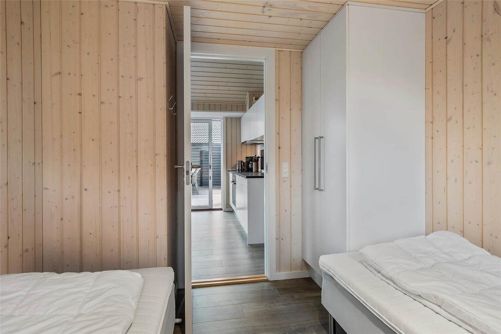 Zwei Betten in einem Raum mit Holzwand. Durchgang zur Küche und Terrasse.