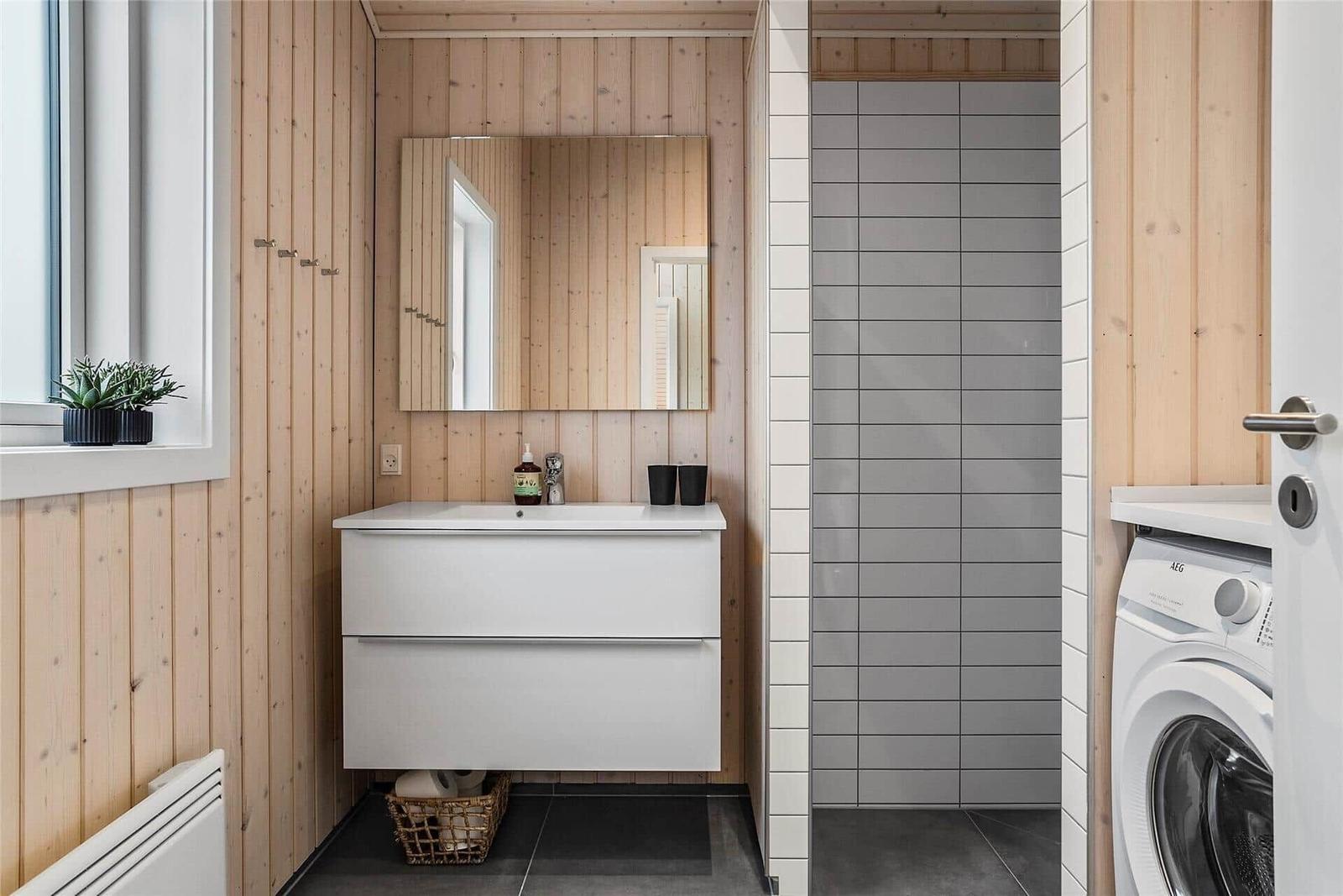 Badezimmer mit Waschbecken, Spiegel, Dusche und Waschmaschine.