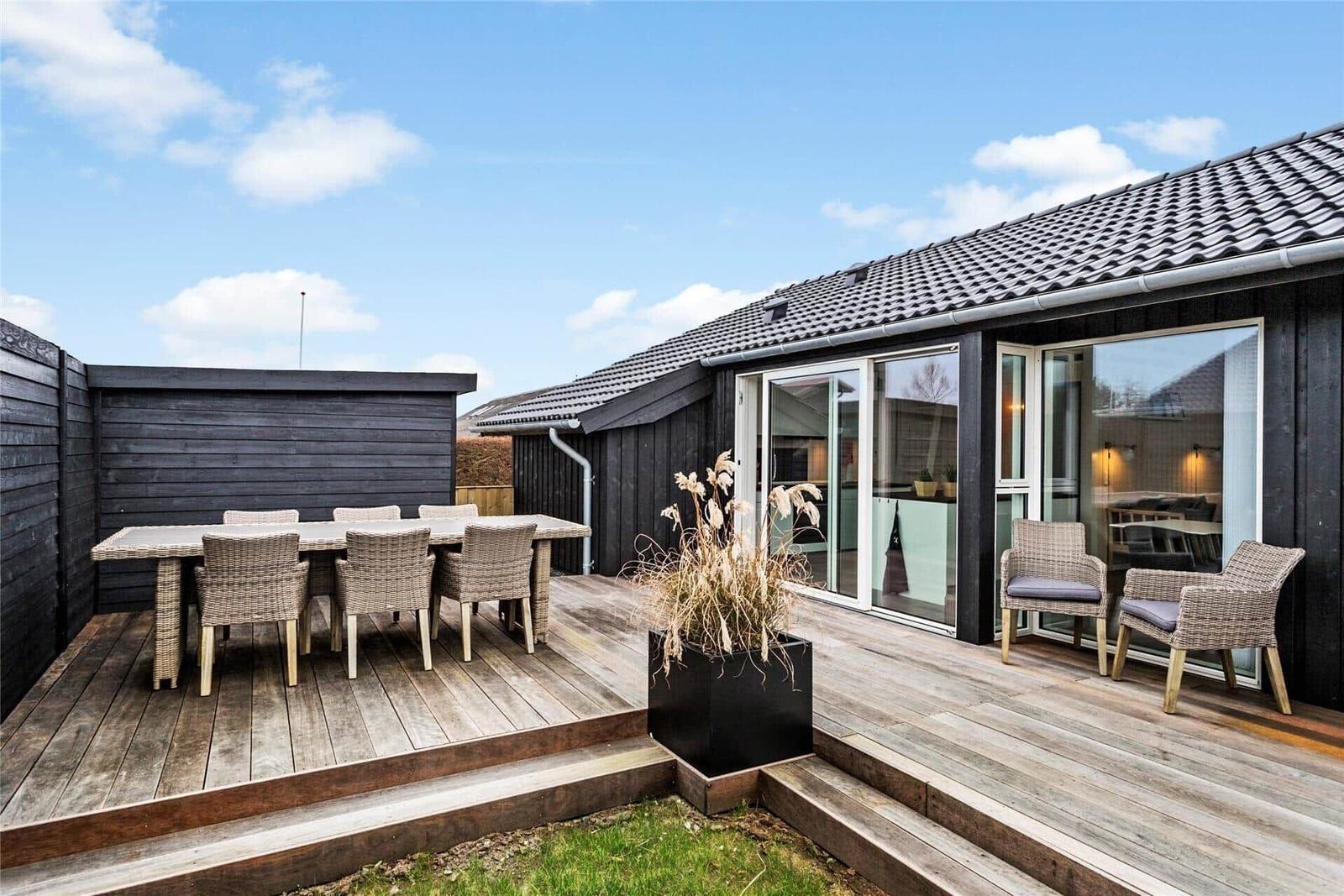 Terrasse mit Sitzgruppe, Tisch und Pflanze vor einem Haus mit Glasfront.