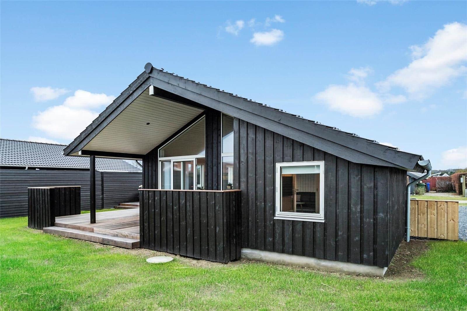 Moderne Holzhütte mit Terrasse und grünem Rasen. Fenster zeigen innere Räume.