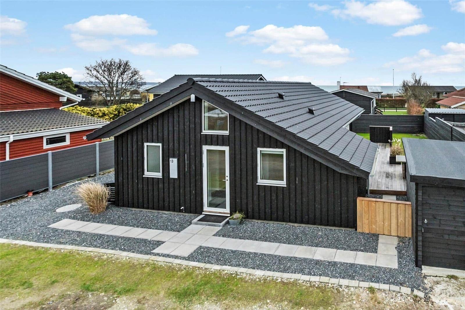 Schwarzes Holzhaus mit Terrasse und Garten. Modernes Design mit weißen Fenstern.