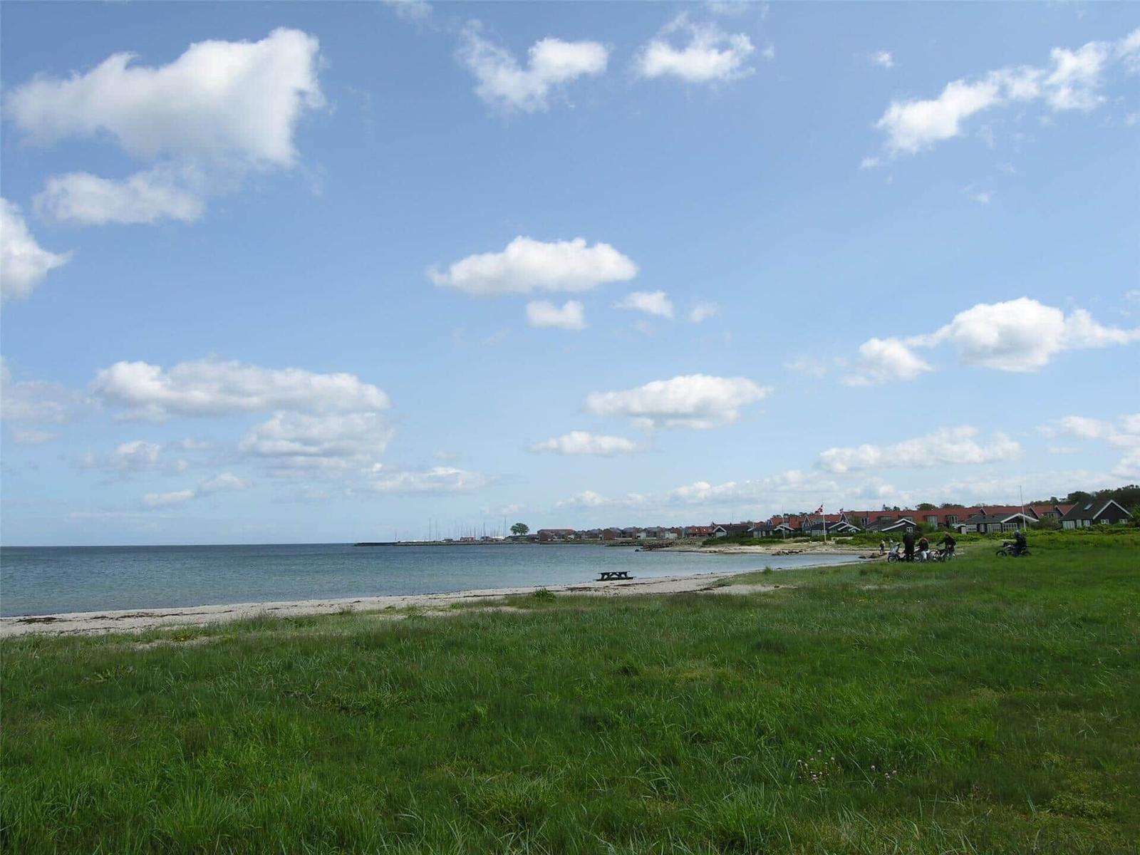 Strand mit Grasfläche und Häusern am Horizont unter blauem Himmel mit weißen Wolken.