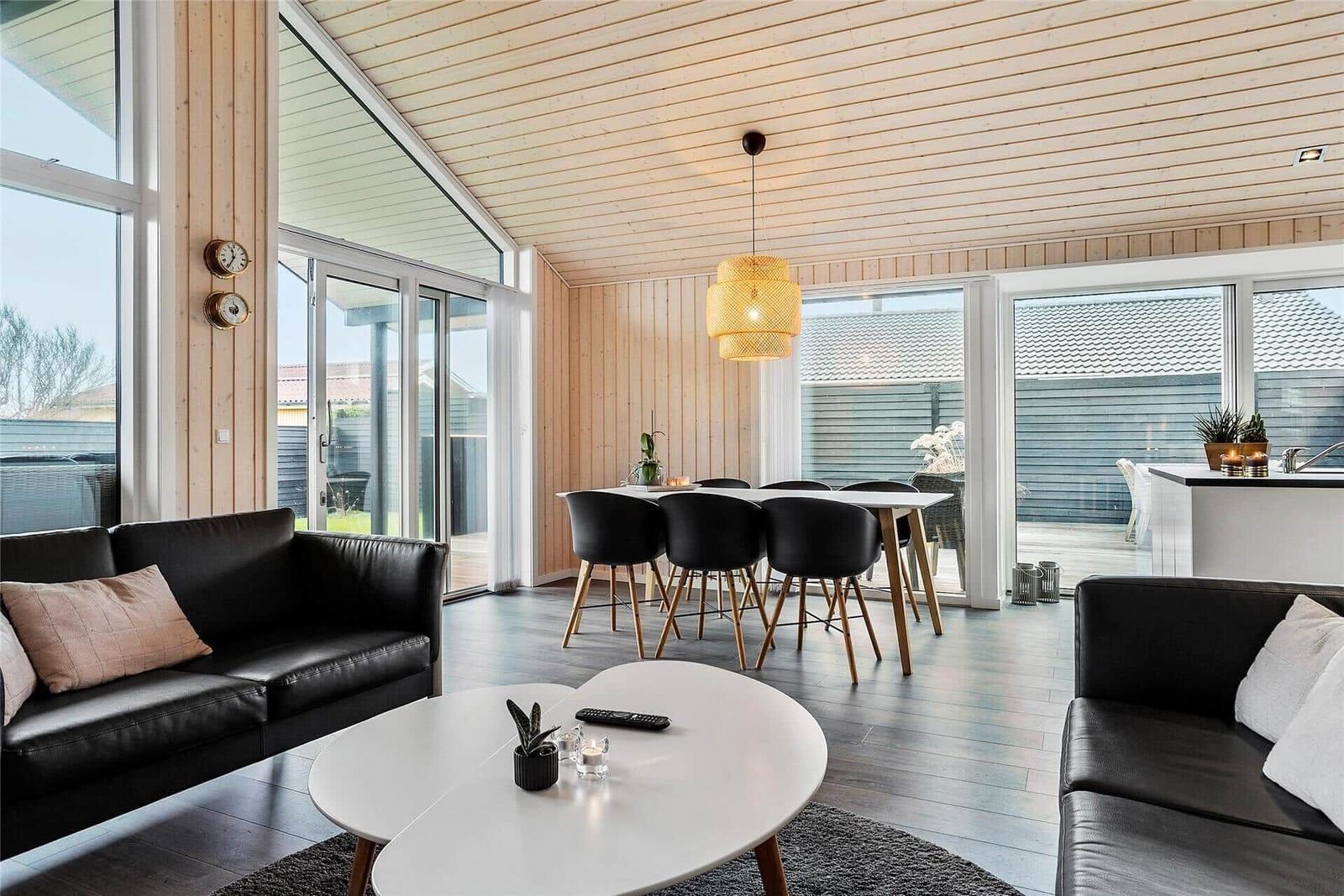 Wohn- und Essbereich mit schwarzen Sofas, weißem Tisch und Holzdecke.