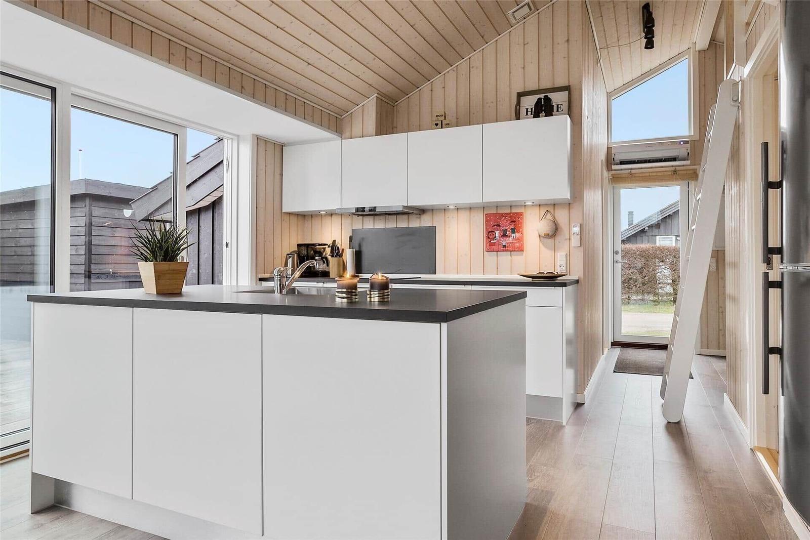 Küche mit weißen Schränken, Holzdecke und Fenstern. Eine Leiter lehnt an der Wand.