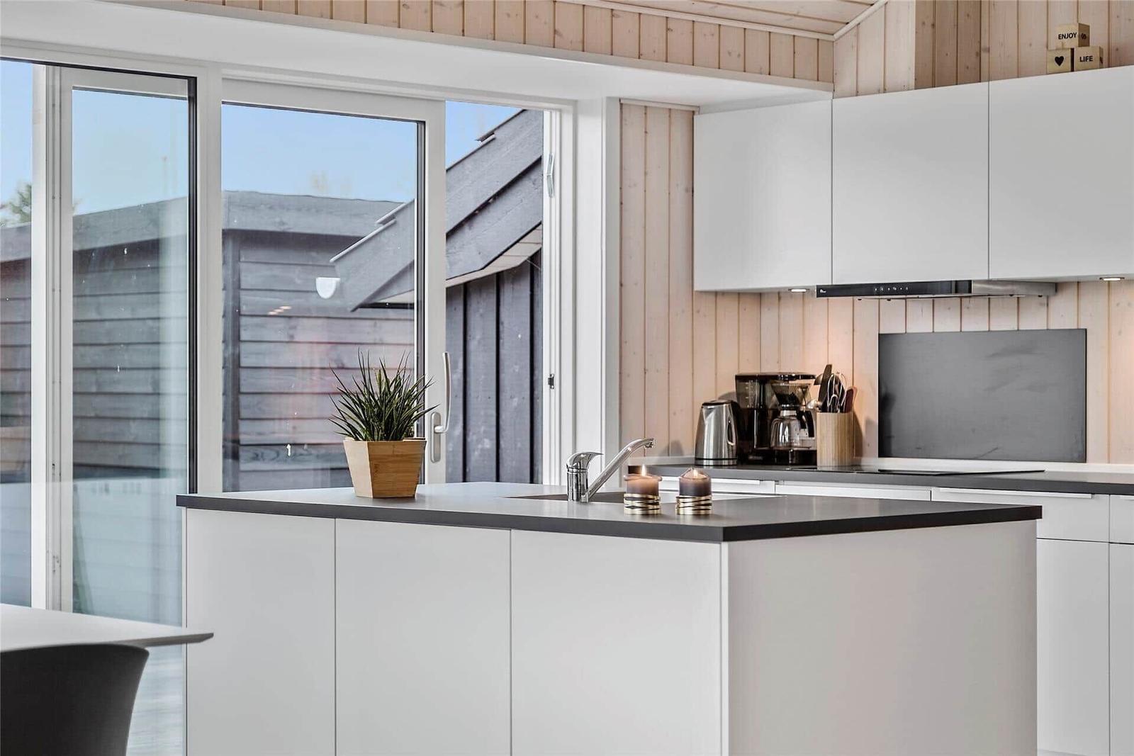 Küche mit weißer Einbauküche, dunklem Arbeitsplatz und Glasfront zur Terrasse.