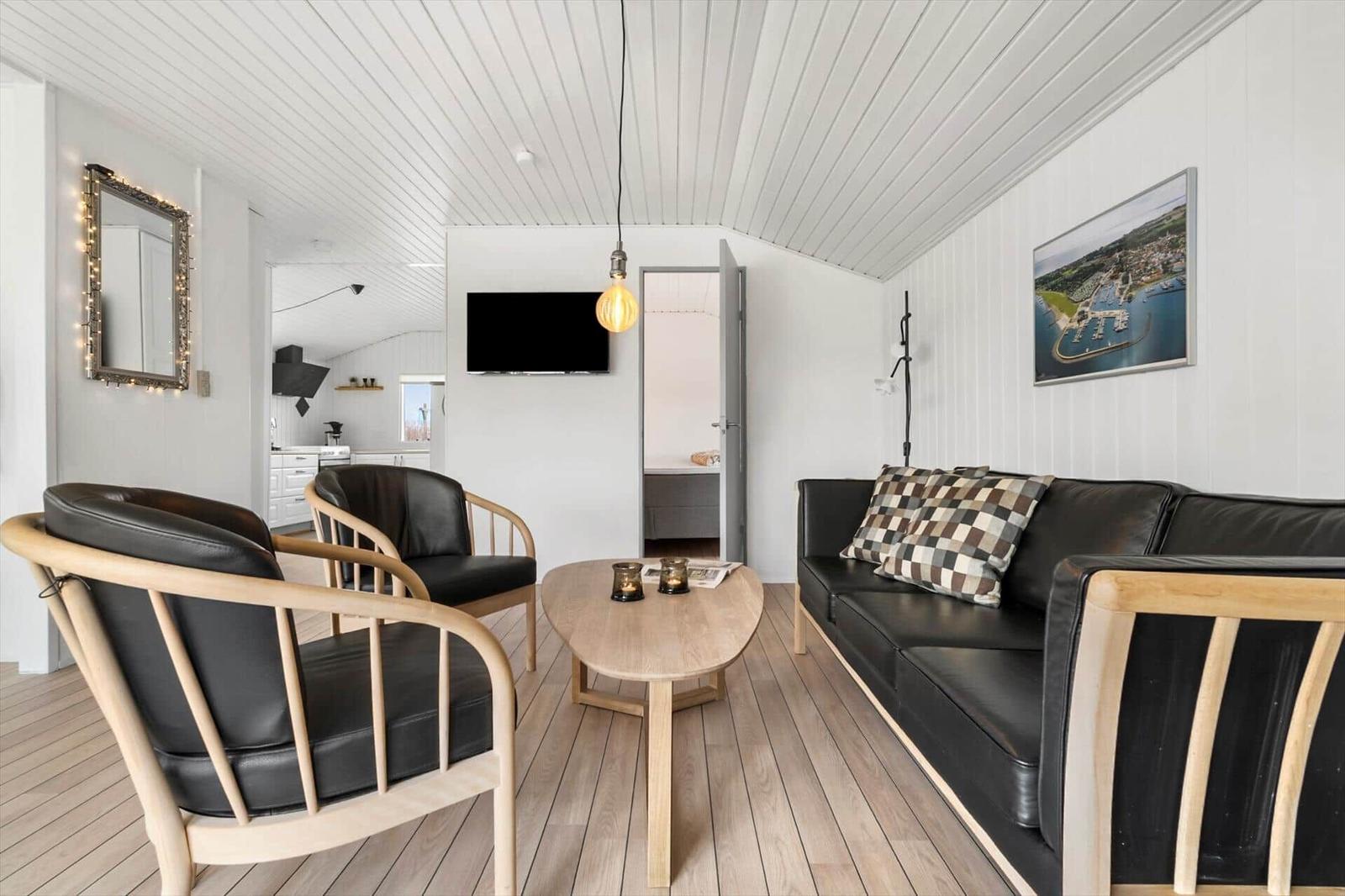 Wohnzimmer mit Sofa, zwei Sesseln und Holztisch. Hintergrund zeigt Küche und Schlafzimmer.