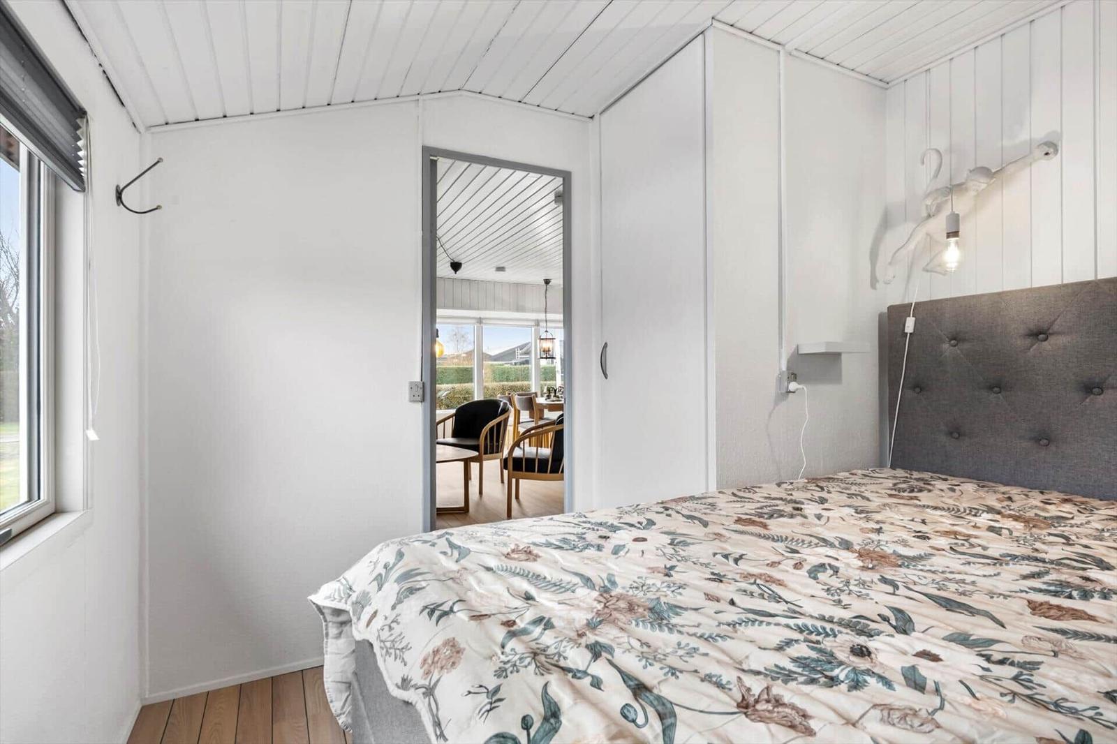 Schlafzimmer mit Bett, Fenster und Blick in Wohnbereich.