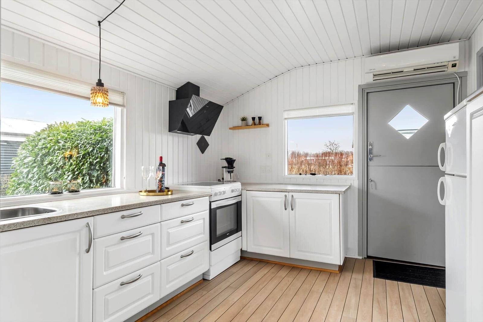 Küche mit weißen Schränken, Holzboden und Fenstern. Küchenzeile mit Herd und Kühlschrank.
