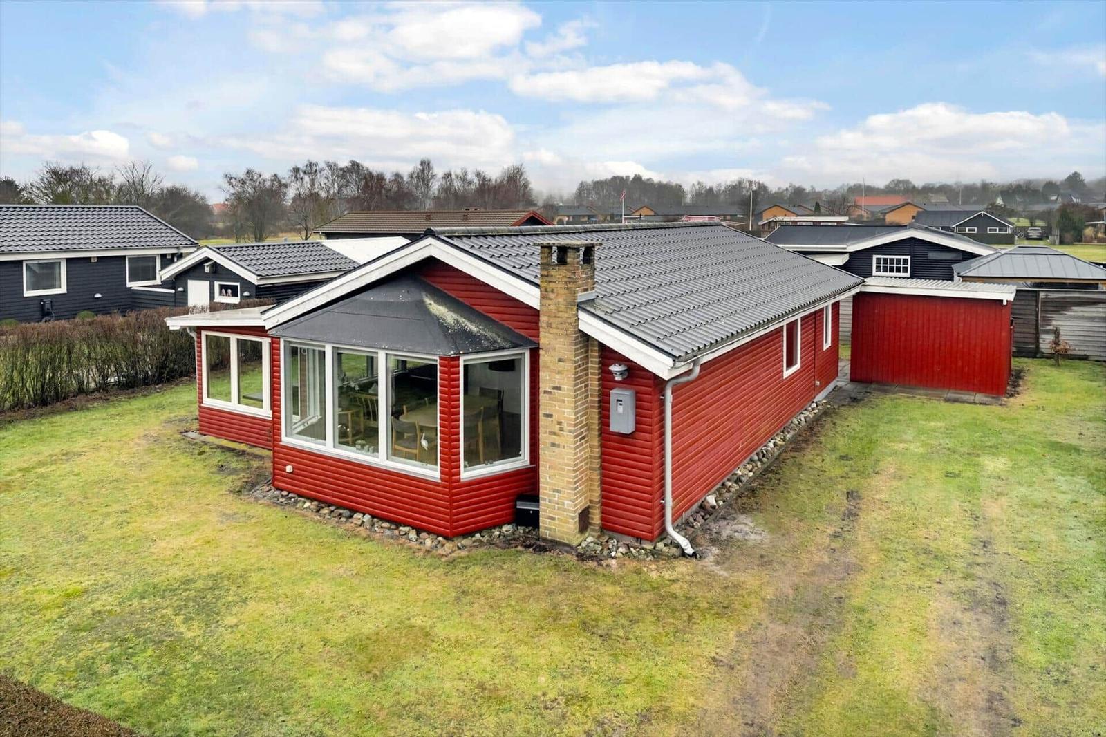 Rotes Holzhaus mit großem Fensterbereich und Garten.