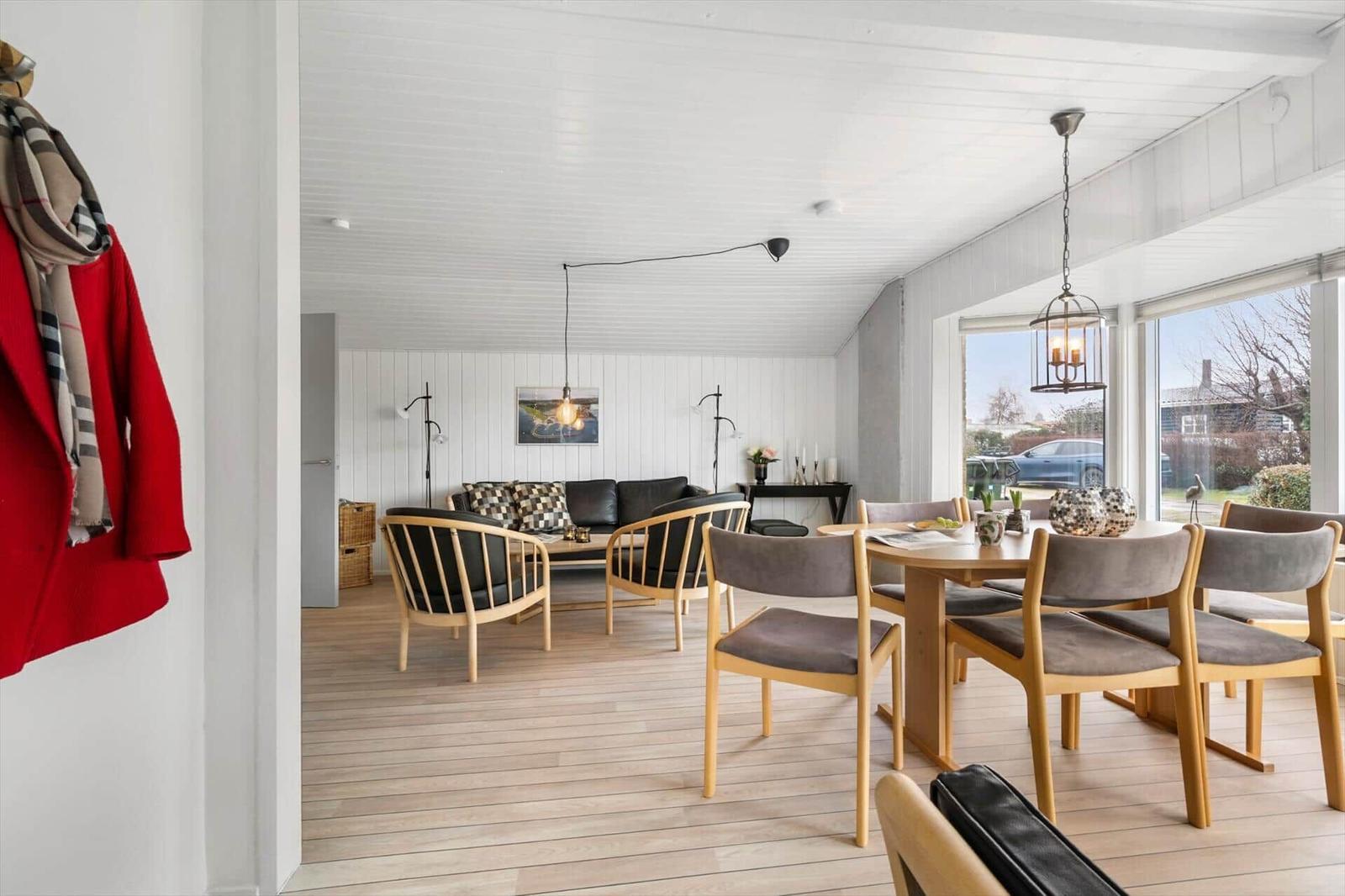 Wohn- und Essbereich mit Holzboden, Sofa, Stühlen und großen Fenstern.