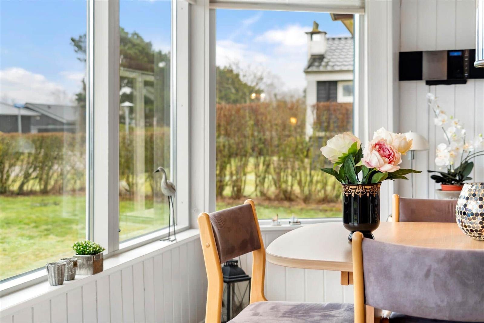 Esstisch mit Stühlen vor großem Fenster mit Blick auf Garten.