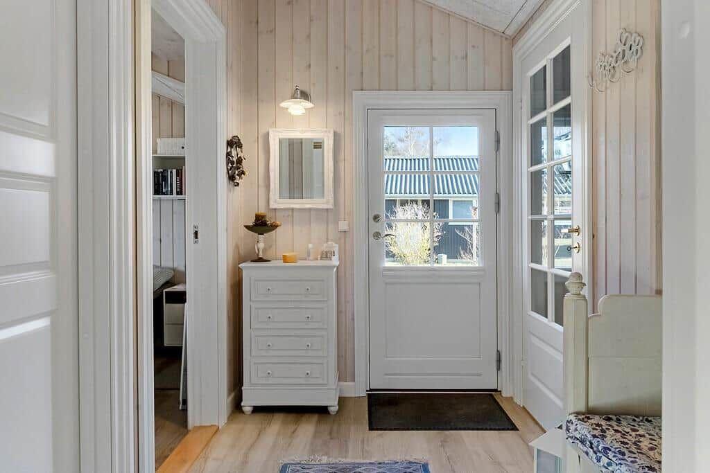 Entryway with white doors, wood-paneled walls, and a vanity. Access to bedroom.