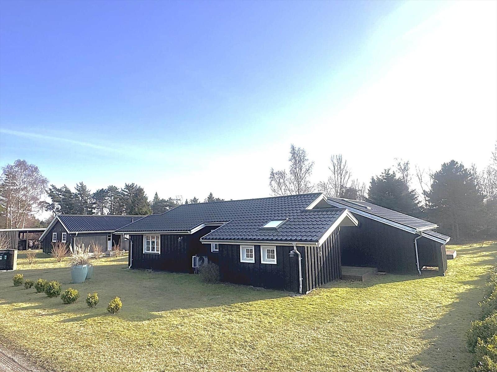 Black wooden house with skylights and solar panels on a green plot.