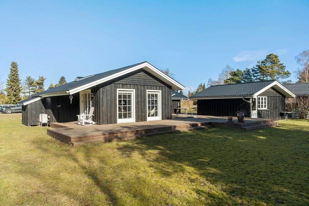 Wooden house with terrace and garden. White windows and door. Background with trees.