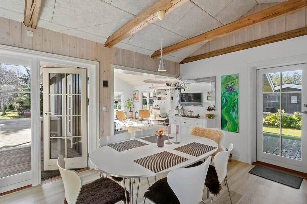 Dining room with round table, white chairs, and wooden beams on ceiling.