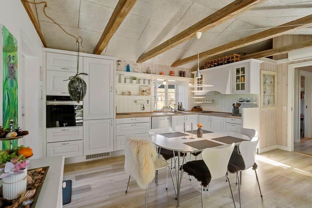 Kitchen with dining area, white cabinets, and wooden beams on ceiling.