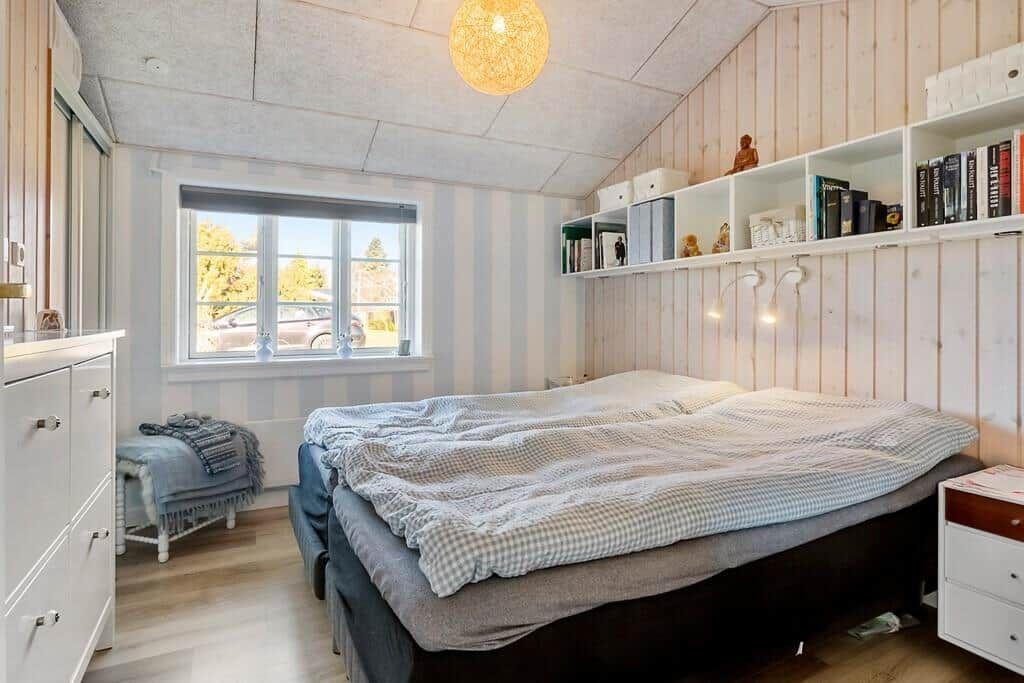 Bedroom with bed, window, and bookshelf on the wall.