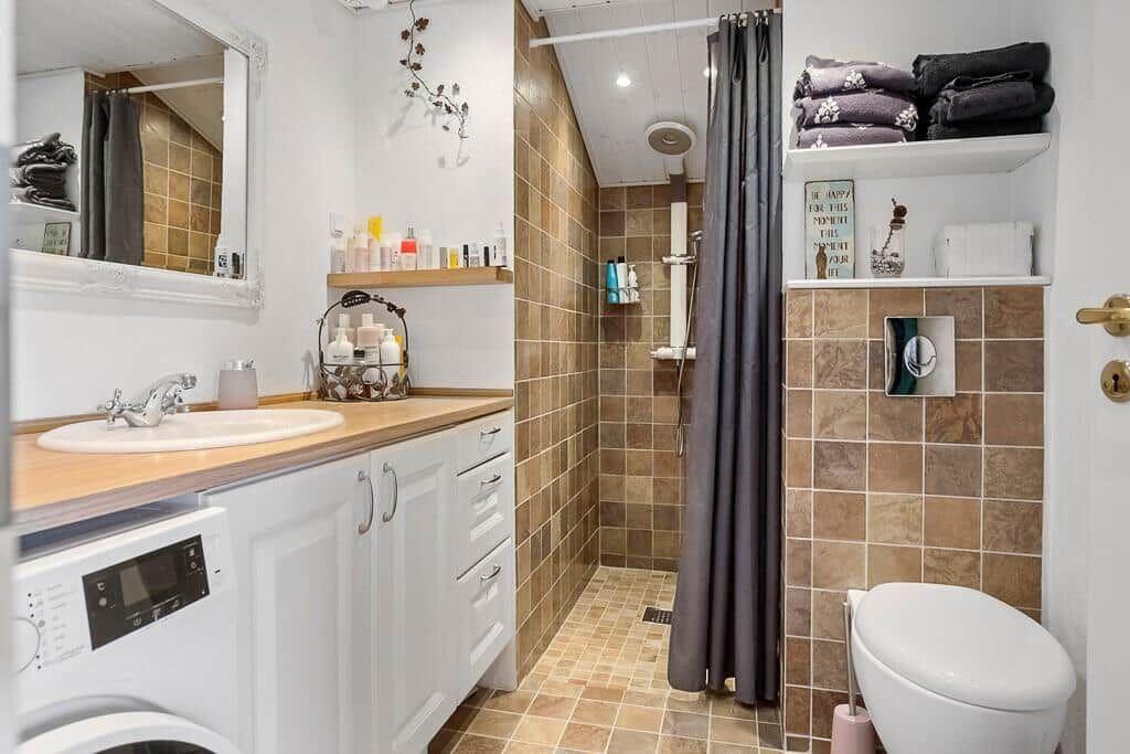 Bathroom with shower, sink, and toilet. Wooden countertop and tiles.