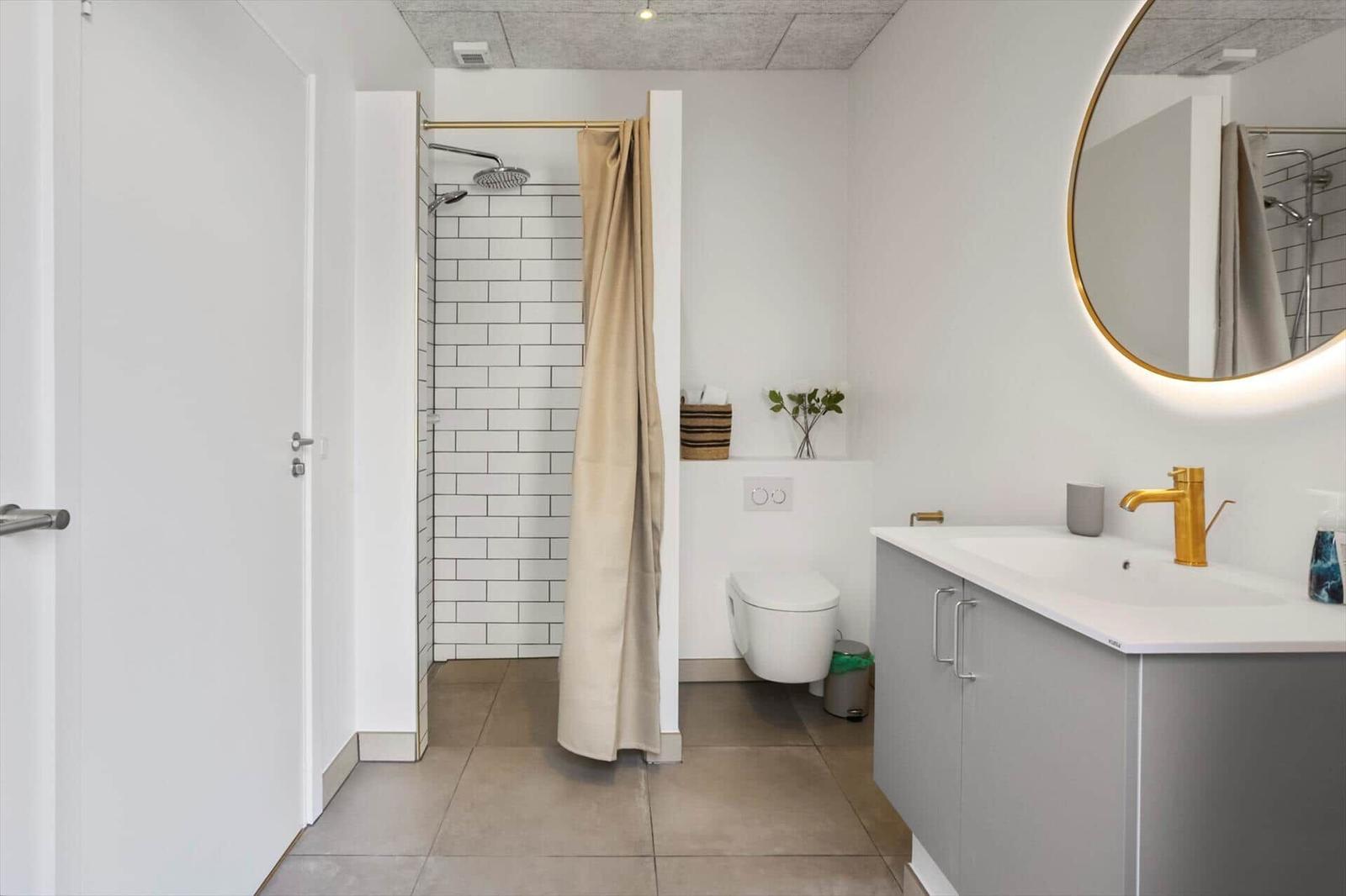 Bathroom with shower, toilet, and sink with gold faucet.