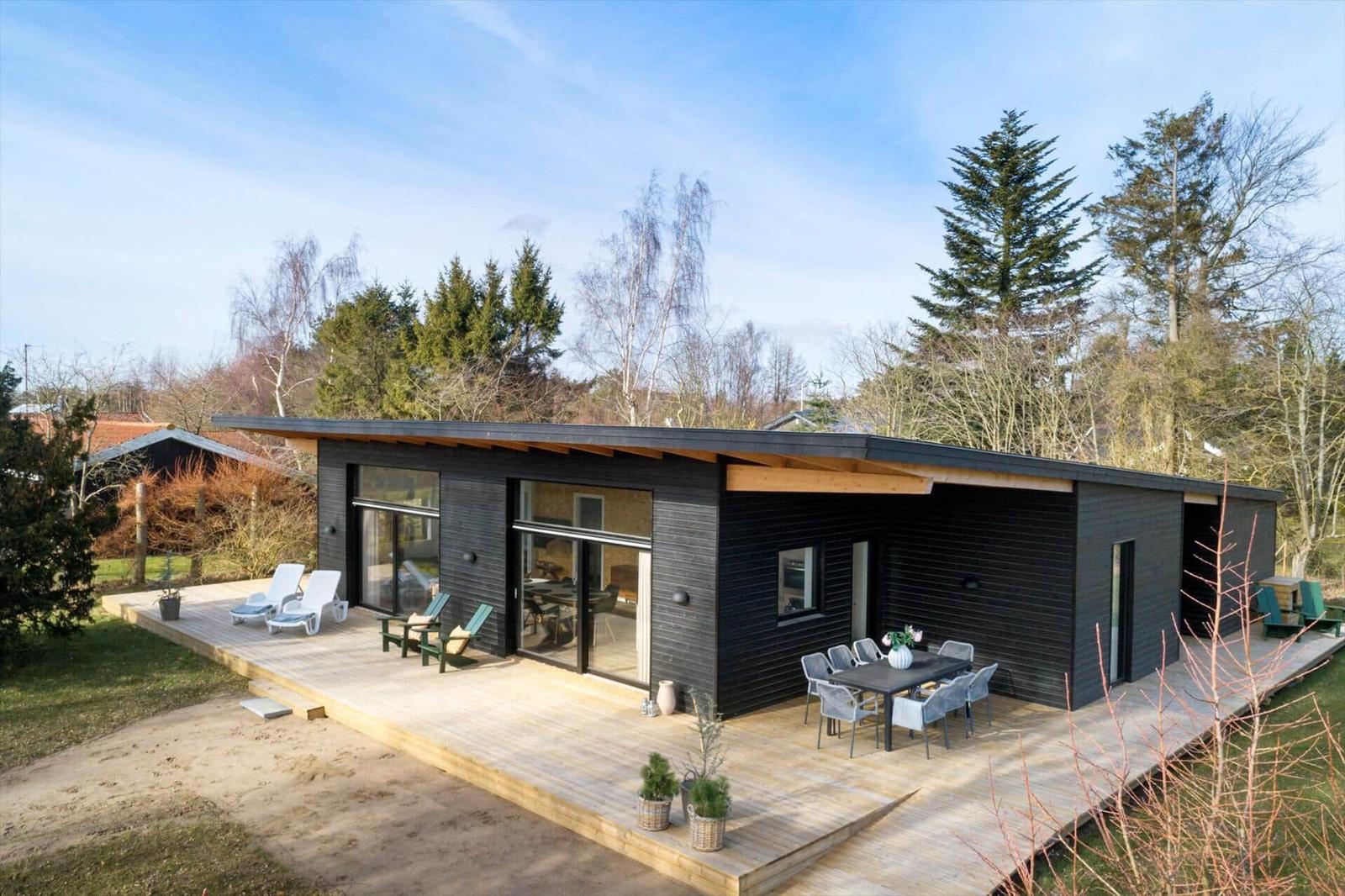 Modern villa with wooden terrace, seating, and view of forest.