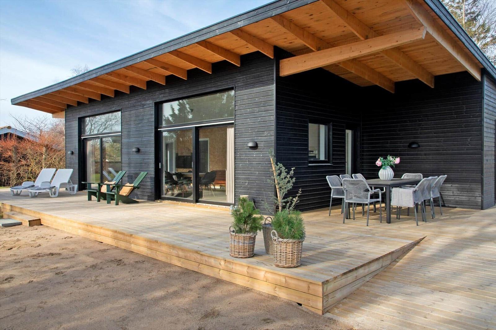 Modern wooden cabin with terrace, garden furniture, and view of the beach.