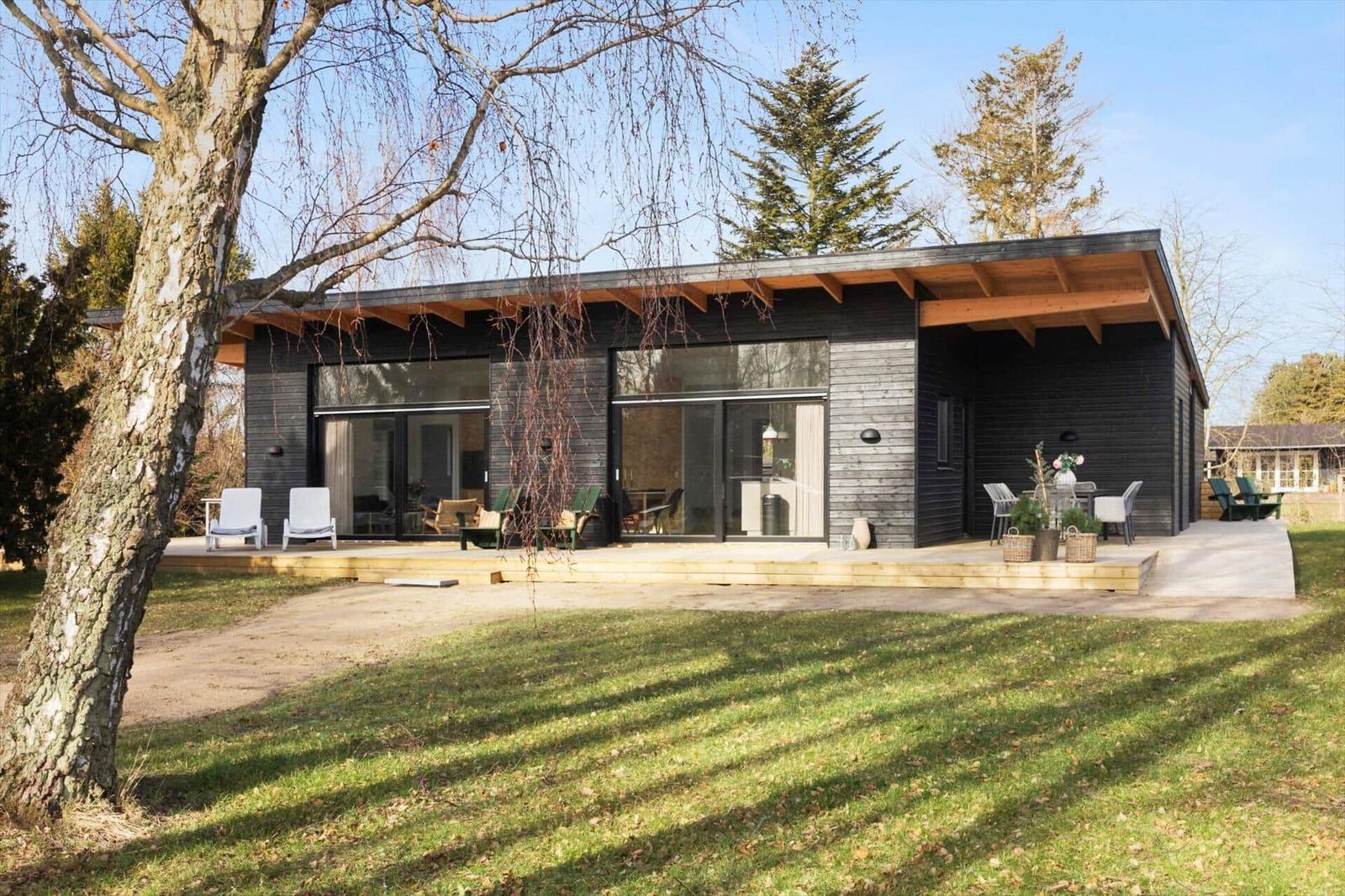 Modern villa with terrace, seating, and surrounding trees.