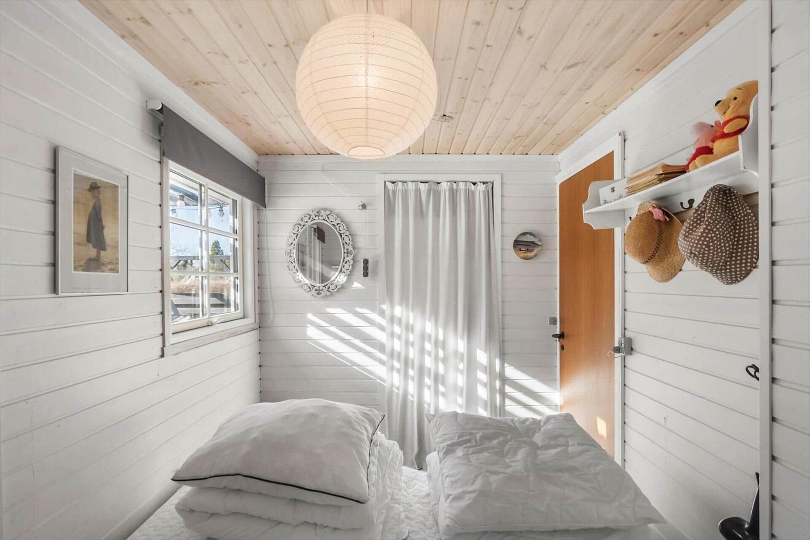 Bedroom with white bed, wooden ceiling, and window. A picture and mirror hang on the wall.