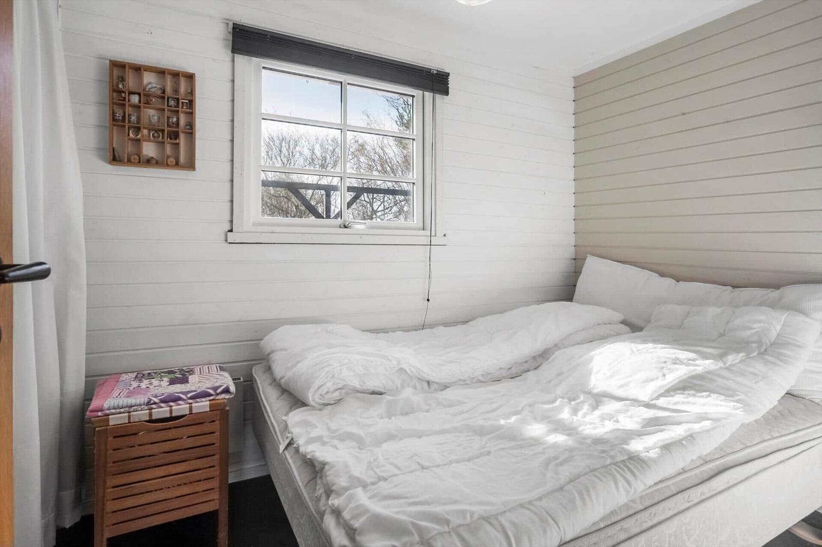Bedroom with bed, window, and wooden shelf on the wall.