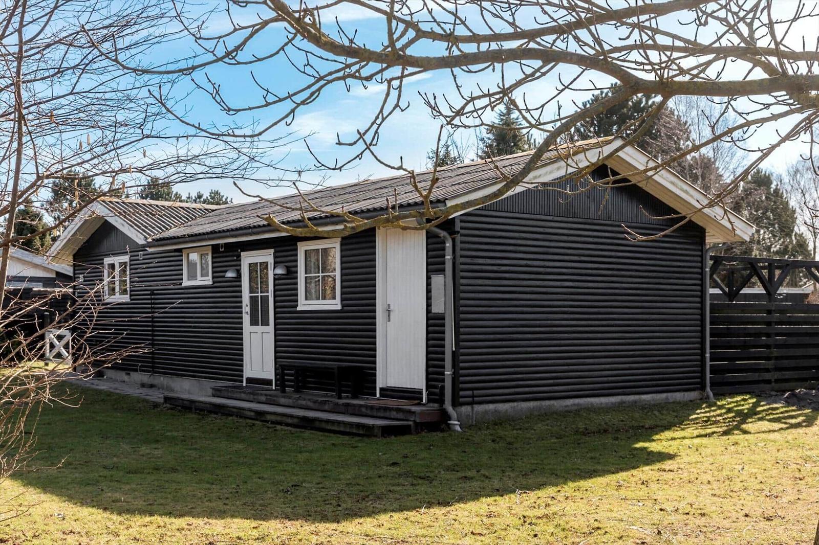 Black wooden house with white doors and windows. Lawn and trees in the background.