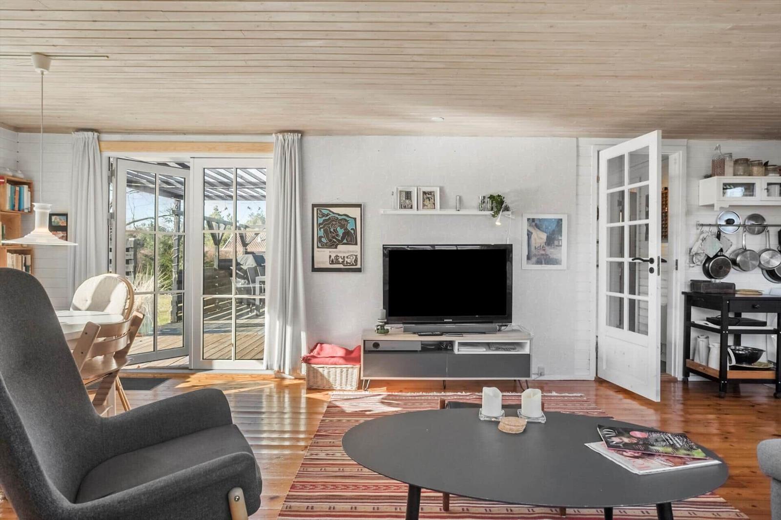 Living area with TV, sofa, and terrace door. Wooden floor and white walls.