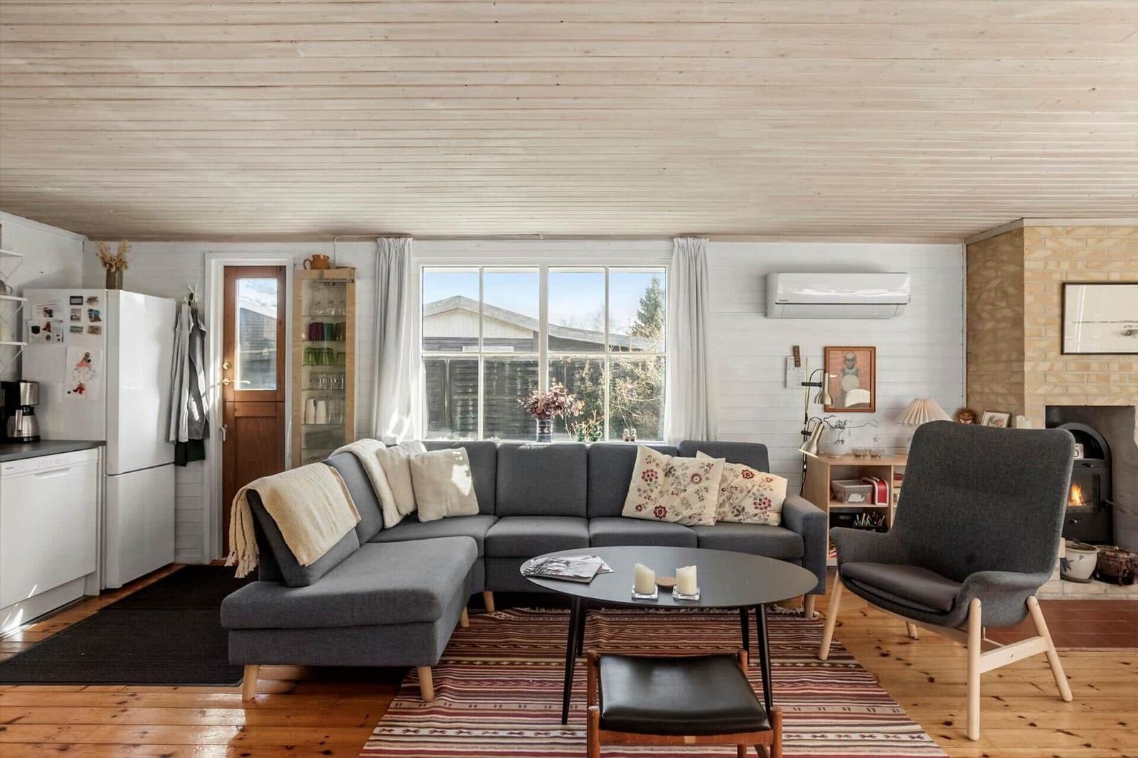 Living room with sofa, armchair, and fireplace. Wooden floor and window view.