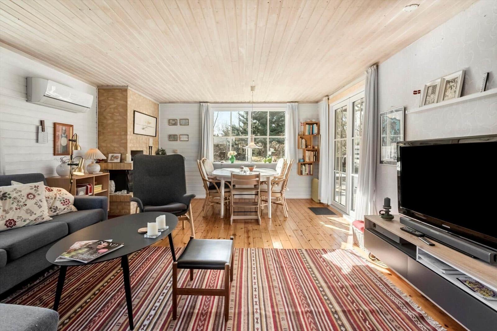 Living and dining area with wooden floor, sofa, TV, and table with chairs.