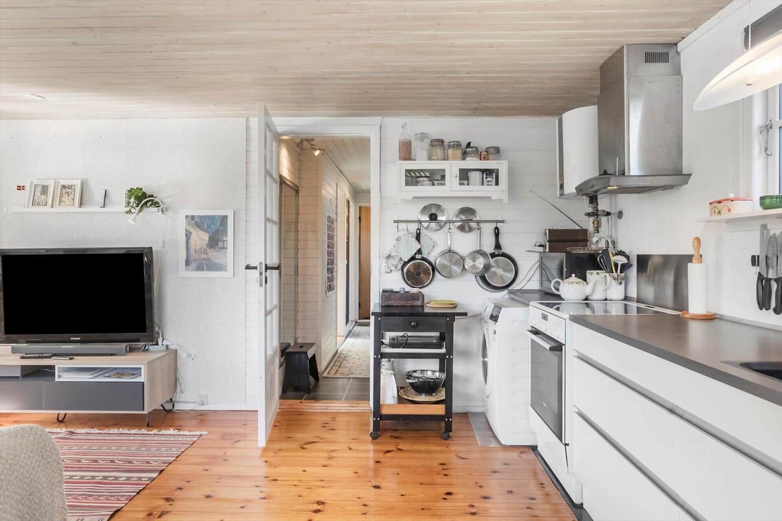 Kitchen with white cabinets and wooden floor. TV, stove, and sink visible.