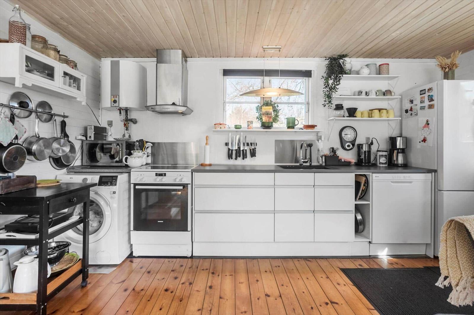 Kitchen with white built-in cabinets, wooden floor, and window. Appliances like dishwasher and refrigerator are present.