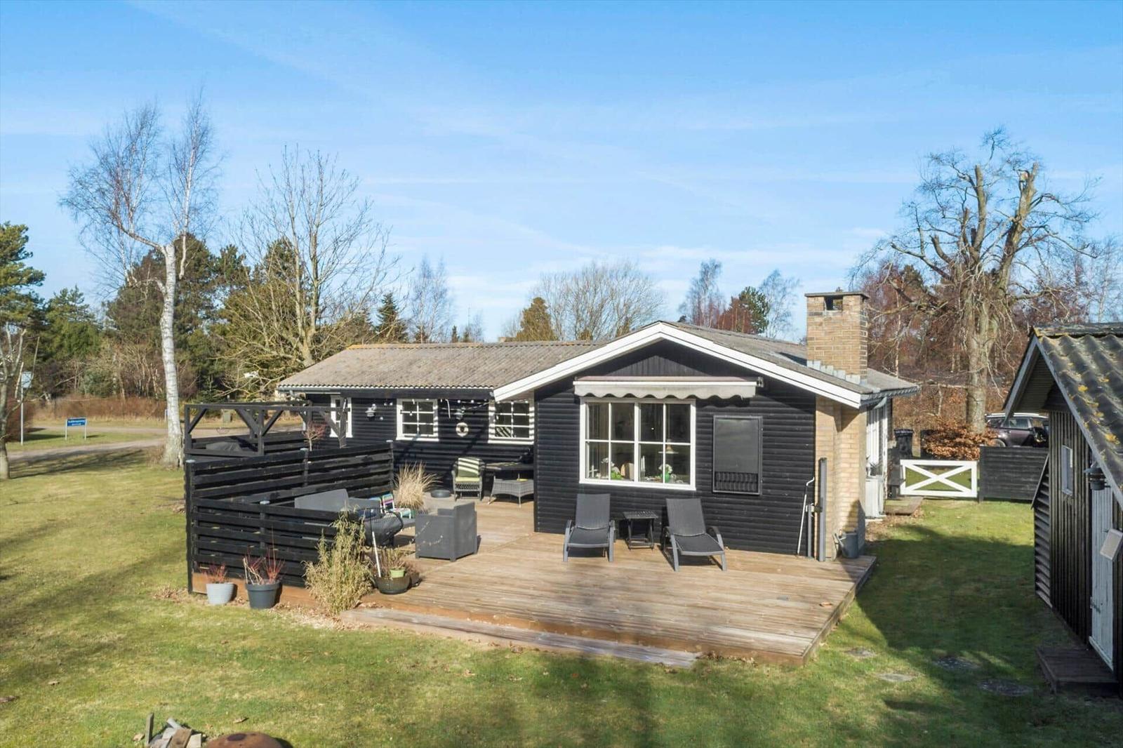 Black house with wooden terrace and garden. Outdoor seating and grill area.
