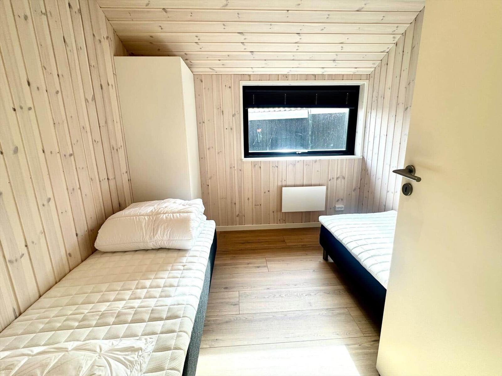 Room with two beds, wooden walls, and a window.
