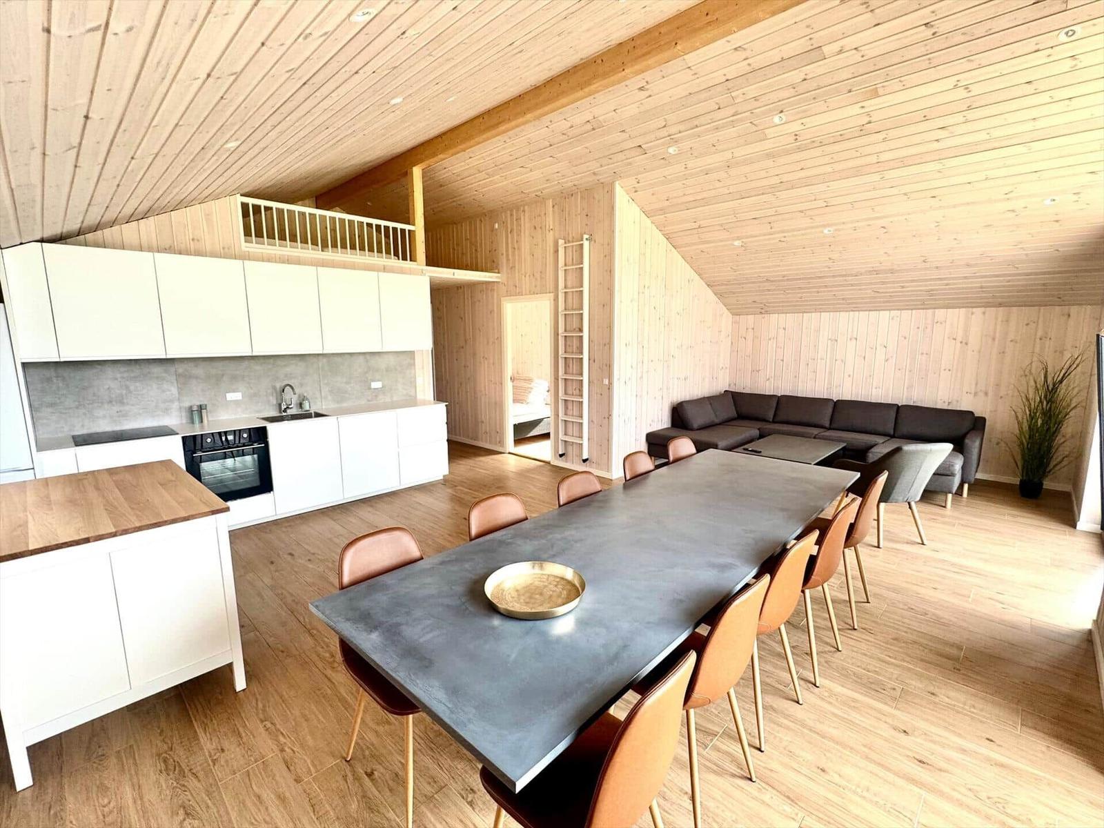 Large dining area with kitchen and living area under wooden ceiling.