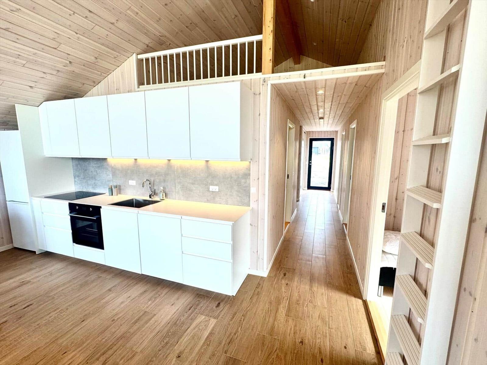 Kitchen with white built-in cabinetry and wooden ceiling. Hallway leads to entrance. Right side has bookshelf.