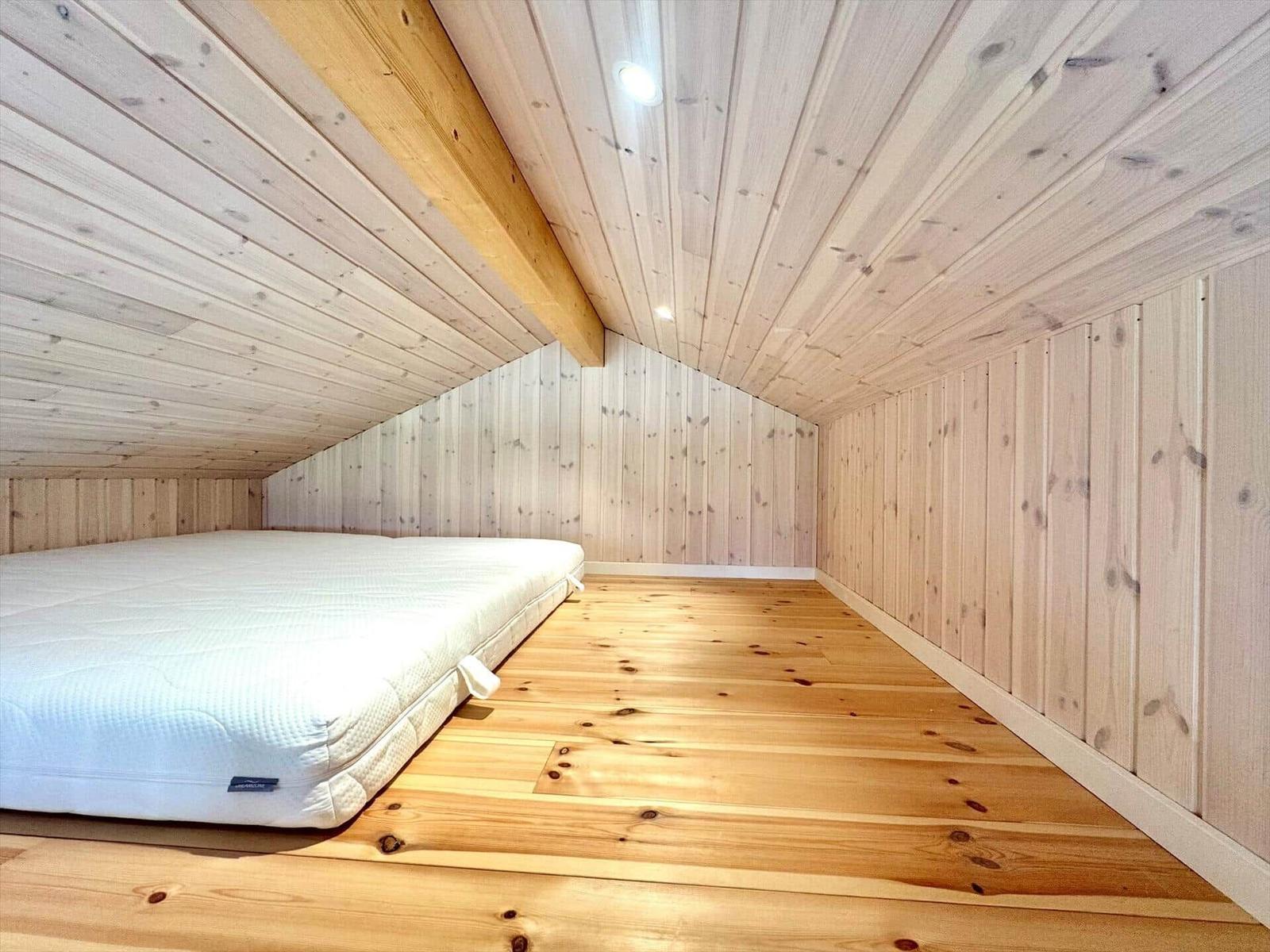 Bedroom with wooden ceiling, walls, floor, and mattress.