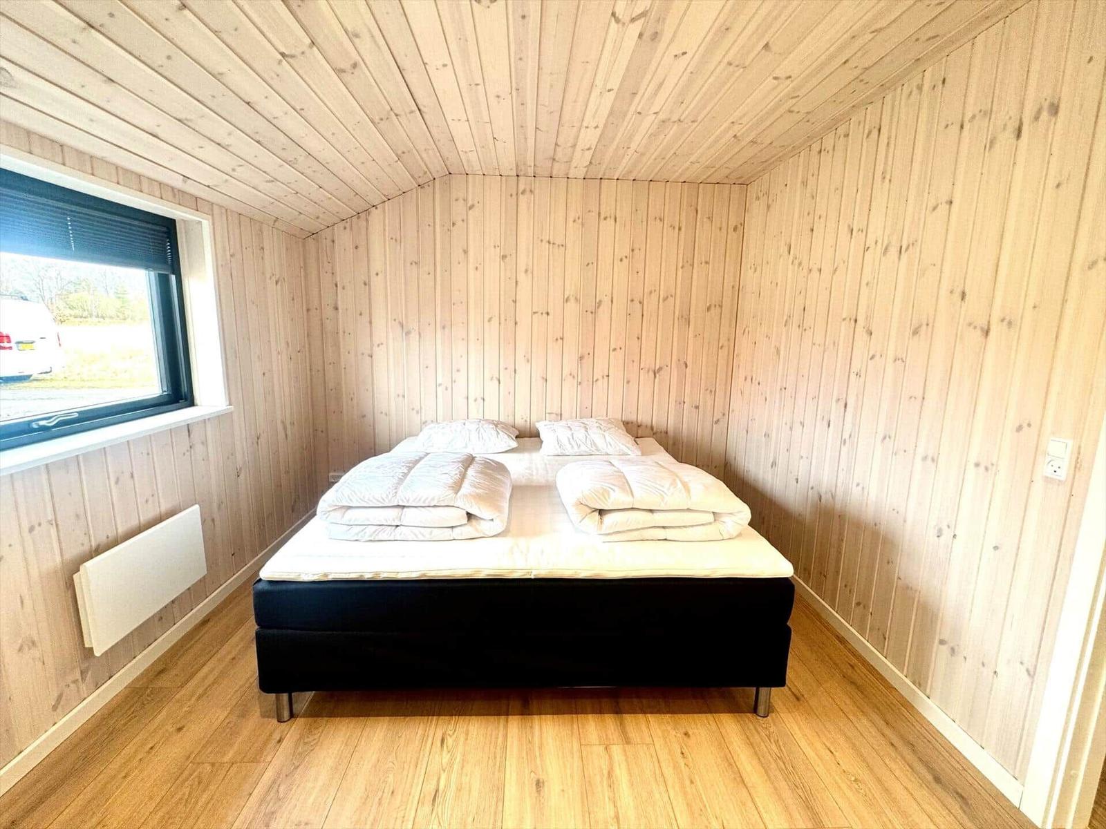 Bedroom with wooden walls and bed with white blankets.