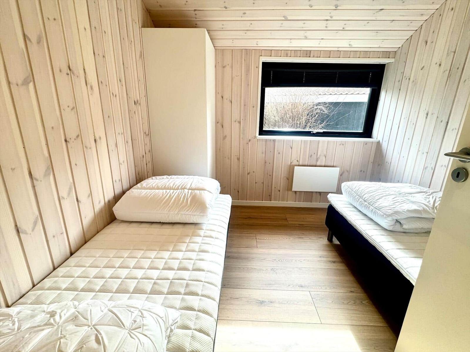 Room with two mattresses, wooden walls, and window