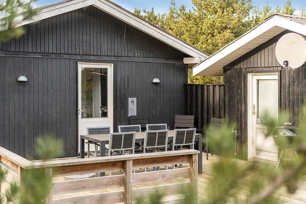 Holzterrasse mit Tisch und Stühlen vor einem schwarzen Holzhaus mit Grill.