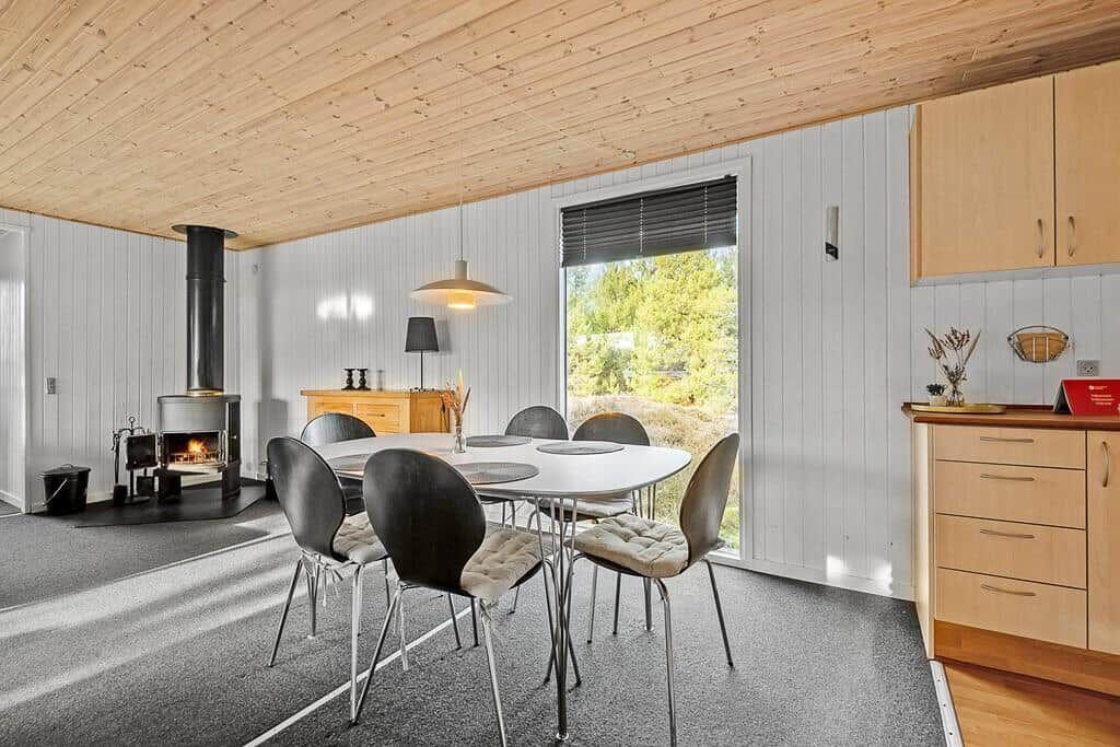 Esszimmer mit Esstisch, Stühlen und Kaminofen. Fenster mit Blick auf Grün.