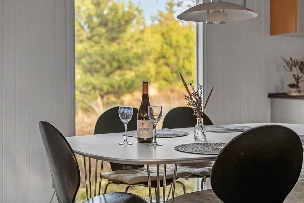 Runder Tisch mit Stühlen und Weinglas vor Fenster mit Blick auf Grün.