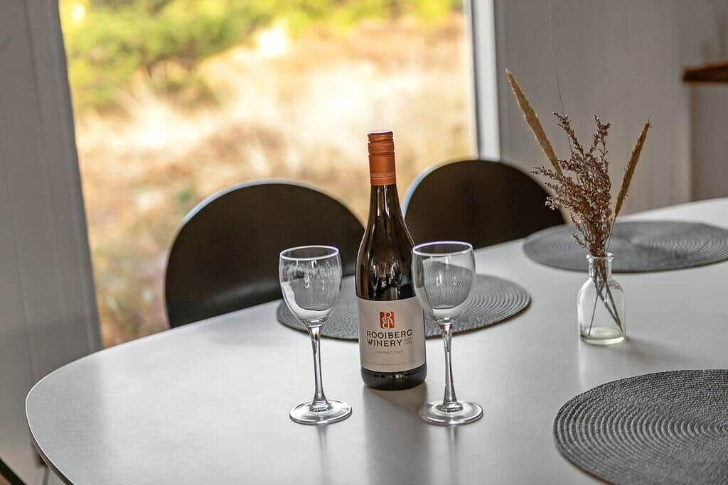 Tisch mit Weinglas, Flasche und Vasenblumen vor Fenster