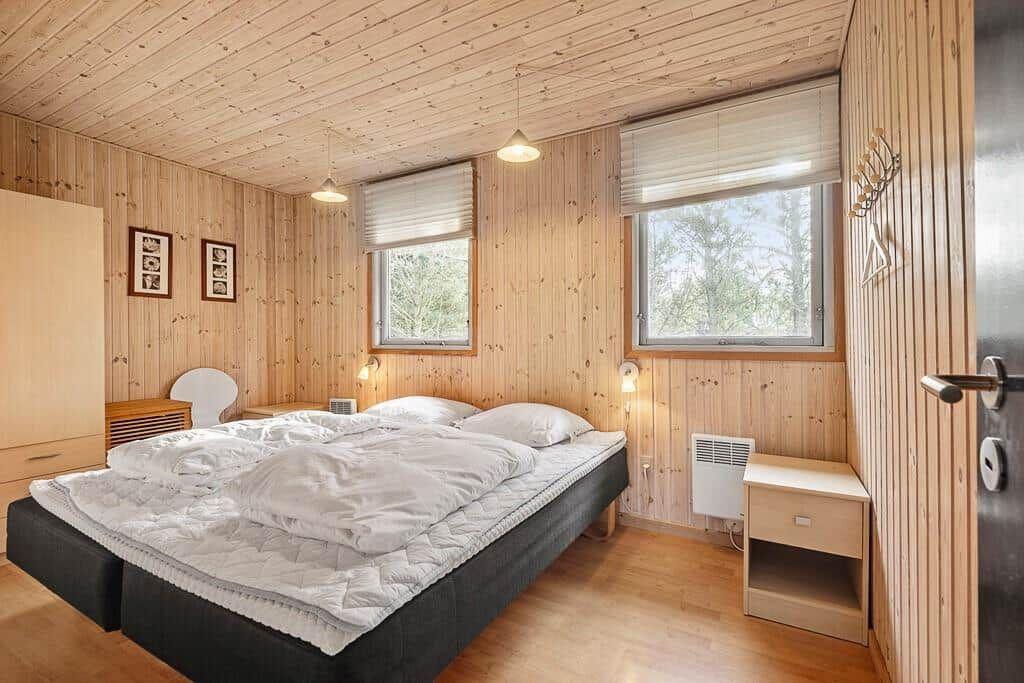 Schlafzimmer mit Holzwandverkleidung, Bett, zwei Fenstern und Nachttisch.